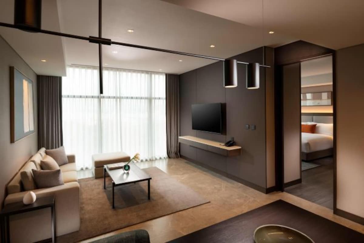 Ett modernt hotellrum med en soffa, ett soffbord, en platt-TV som är monterad på väggen och ett stort fönster med gardiner.