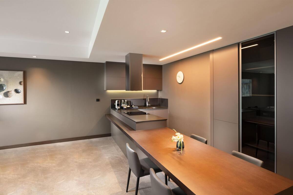 A modern kitchen with a built-in island, a dining area with a wooden table, and a large window.