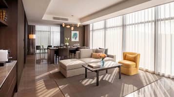 Ein modernes Hotelzimmer mit Essbereich, einer Sofagarnitur, einem Couchtisch mit Vase und großen Fenstern.