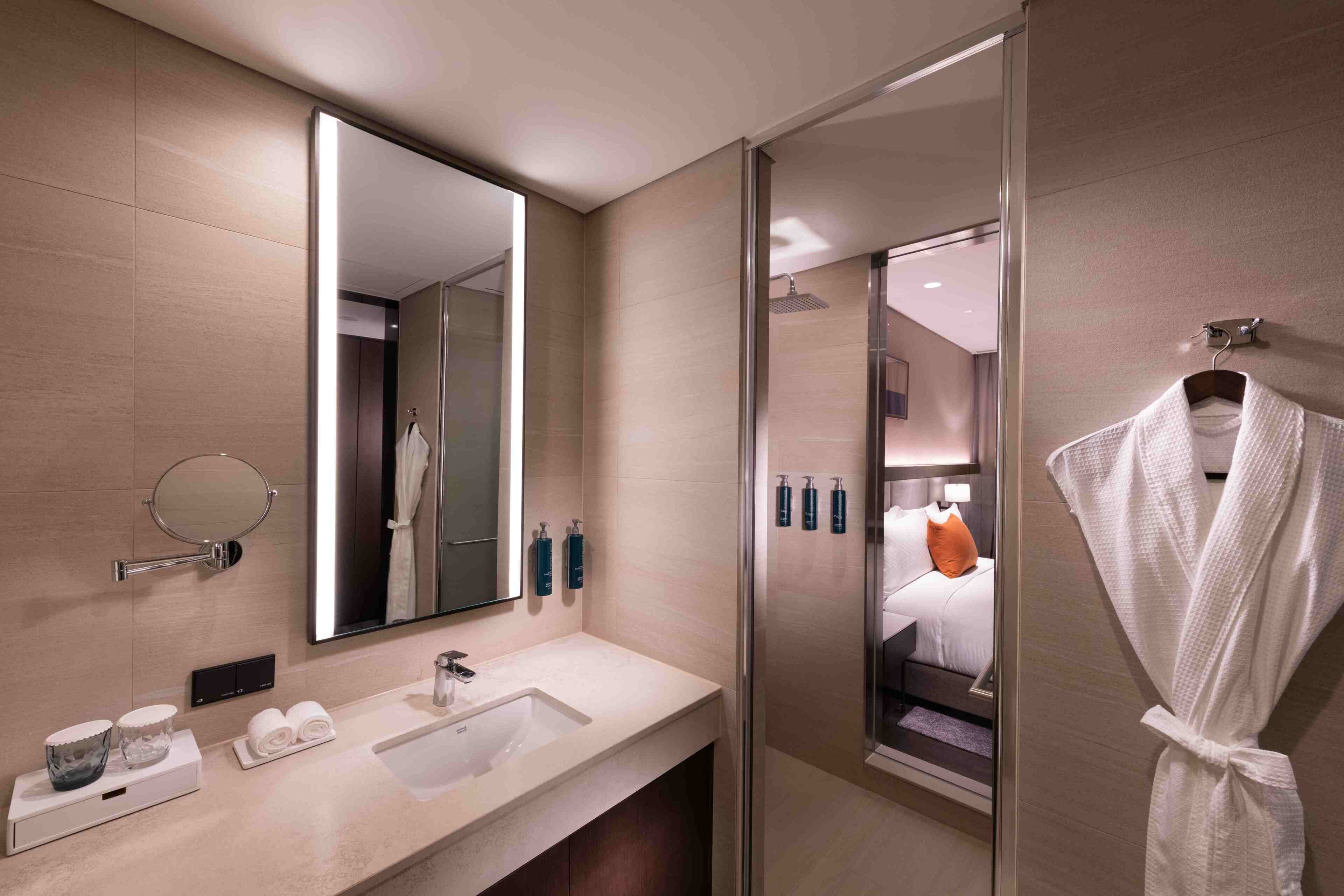A modern bathroom with a large mirror, a sink, a glass shower enclosure, and a robe hanging on a hook.