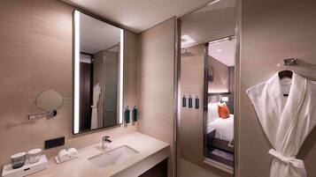 A modern bathroom with a large mirror, a sink, a glass shower enclosure, and a robe hanging on a hook.