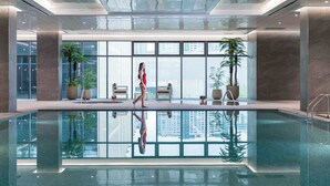 Una piscina interior moderna amb sostre de vidre, finestres grans i plantes en testos.