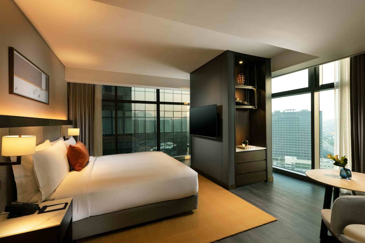 Una habitación de hotel moderna con una cama grande, un televisor de pantalla plana, un escritorio con una silla y un ventanal con vistas a la ciudad.