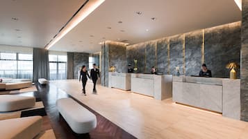 A modern hotel lobby with a reception desk, seating area, and large windows.
