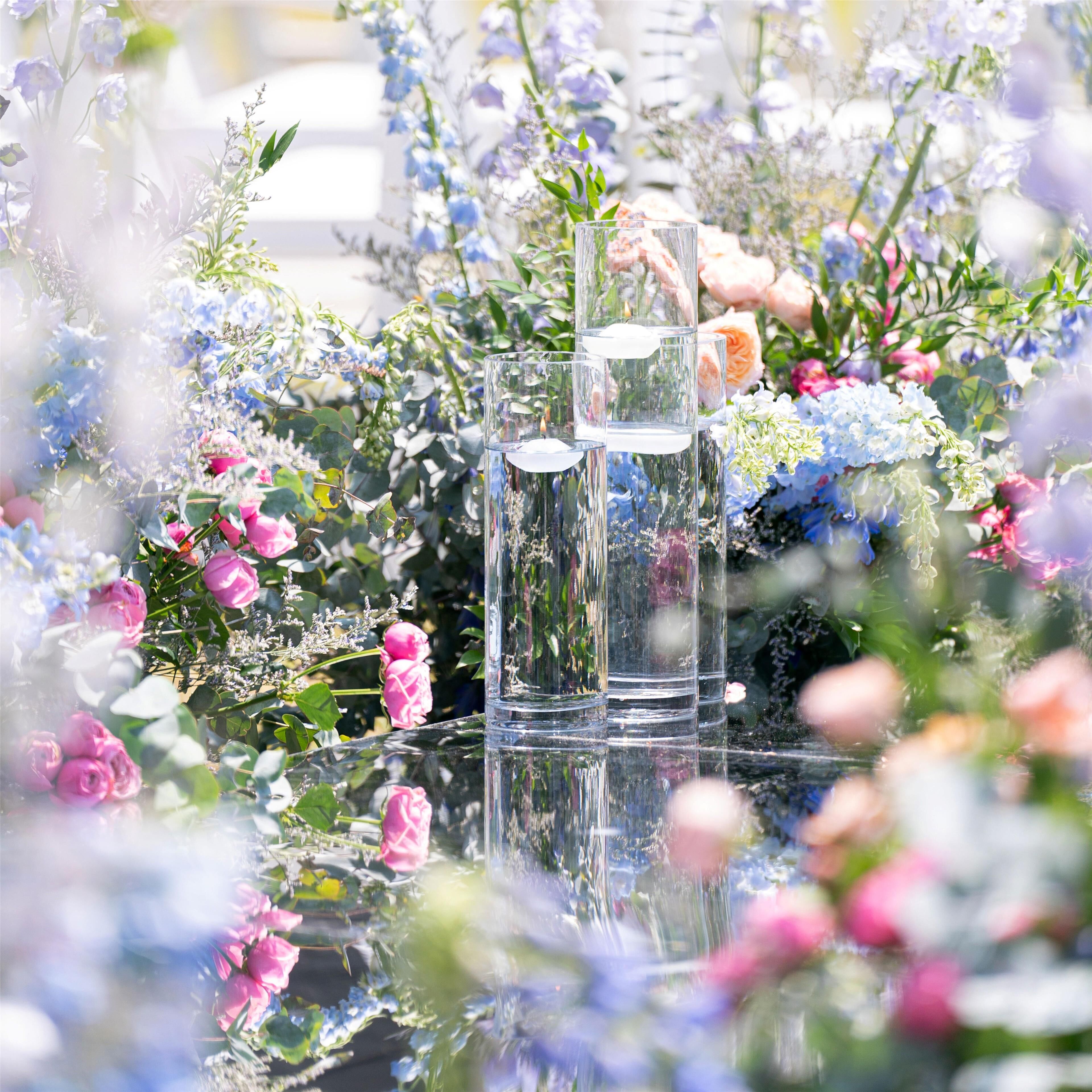 A table with clear glass vases and water, surrounded by various flowers.