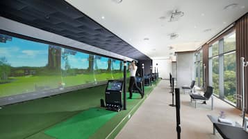 A modern indoor golf simulation room with a large screen displaying a golf course, a golf cart, and a control panel.