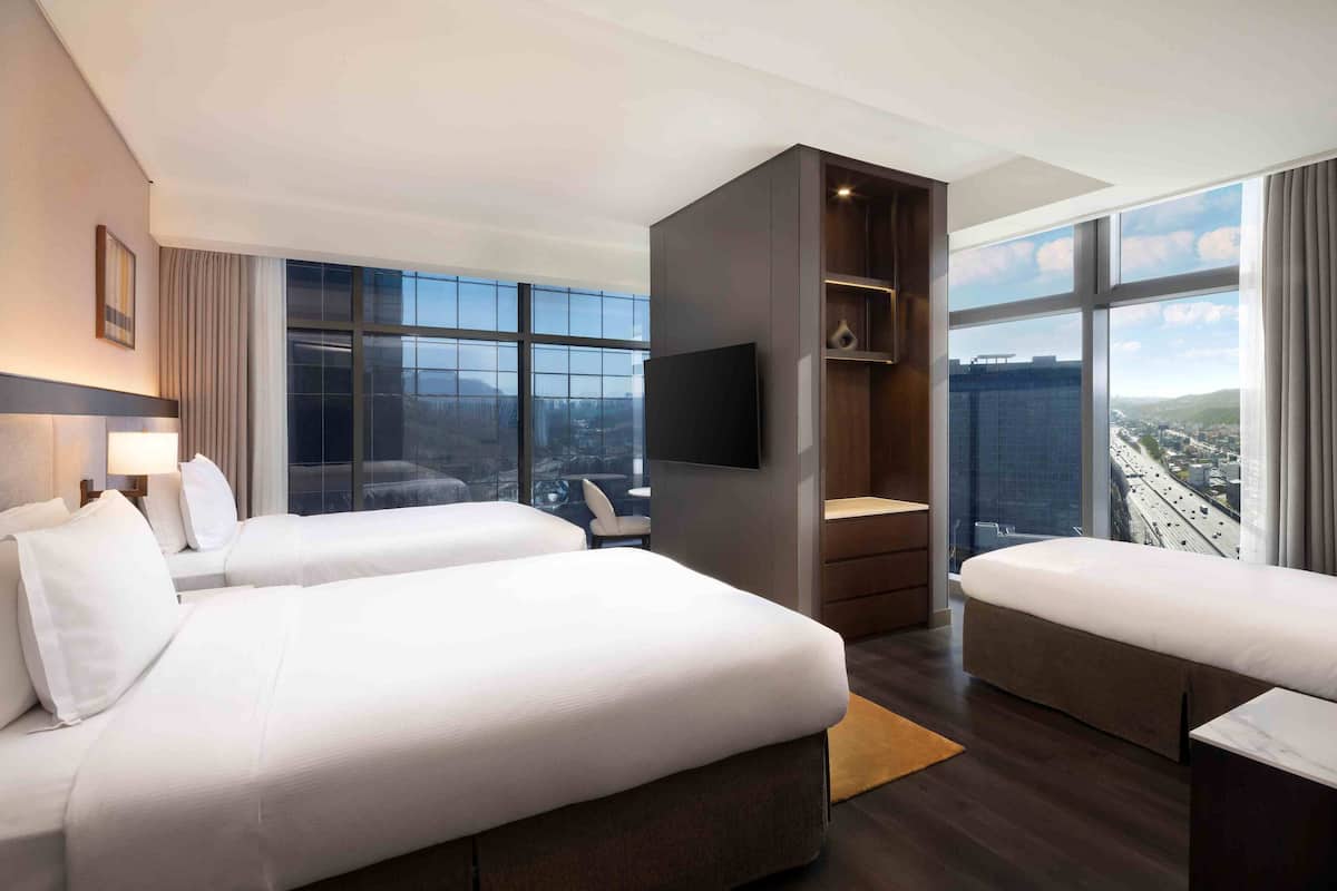 Habitación de hotel con dos camas, televisión, escritorio, silla y un ventanal con vistas a la ciudad.