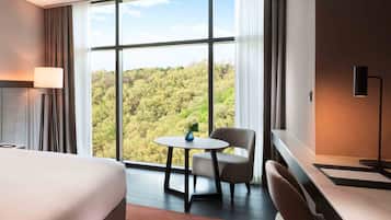 Habitación de hotel con un ventanal grande, una cama, un escritorio, una silla y una lámpara.