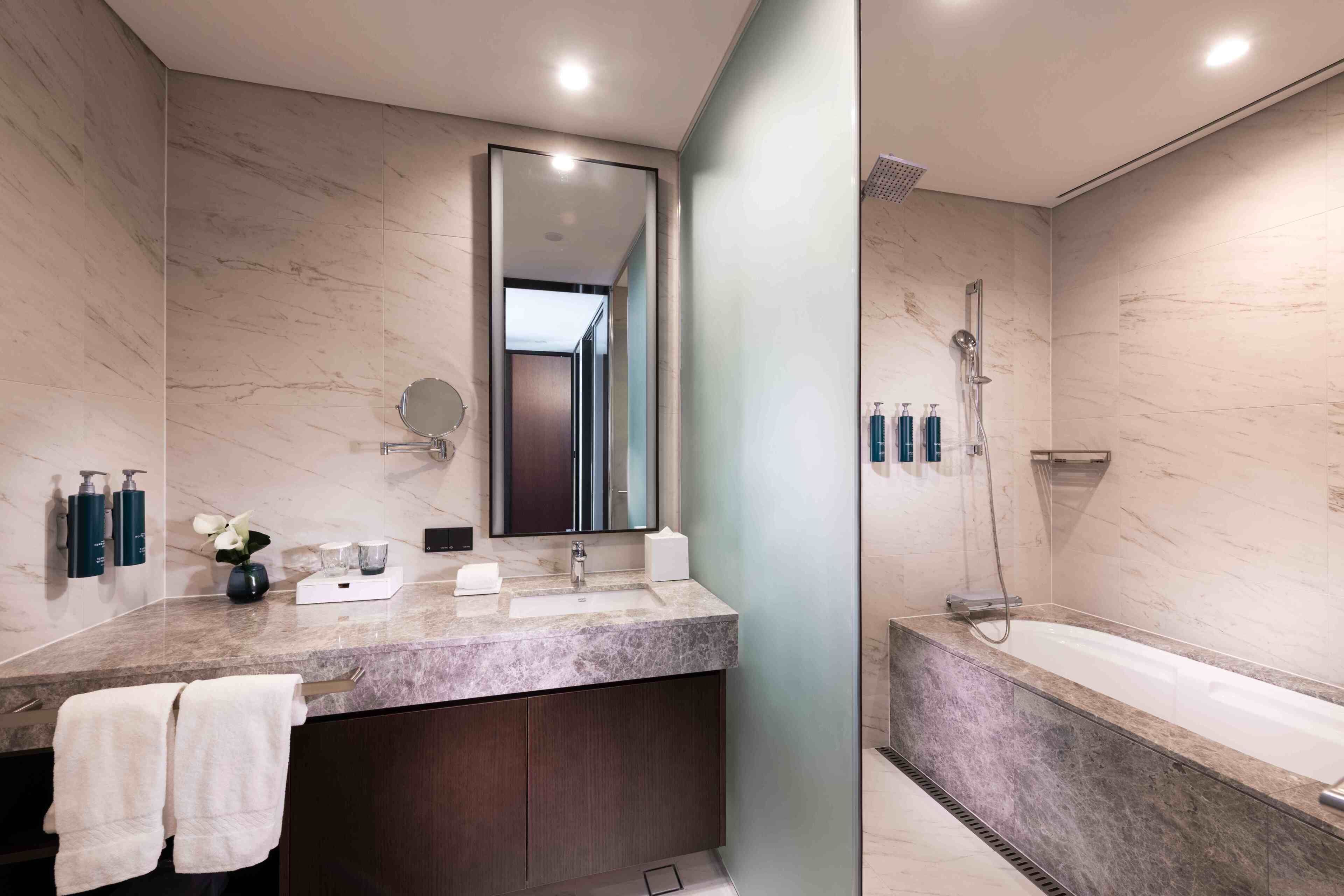 A modern bathroom with a marble vanity, a large mirror, a bathtub, and a shower.