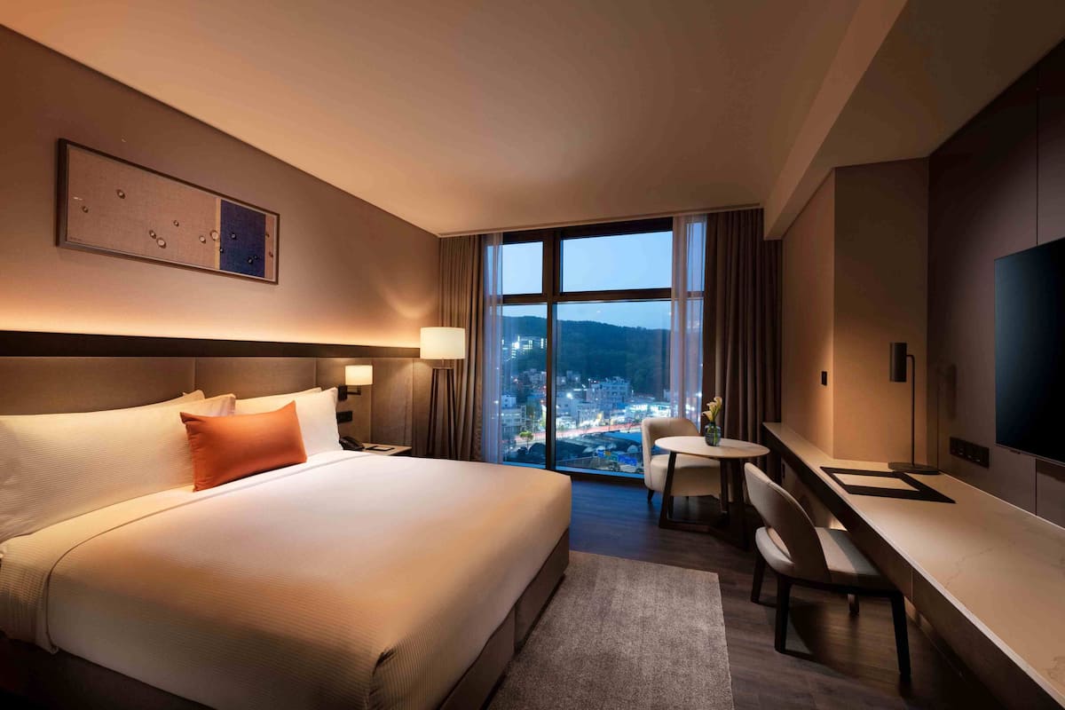 Una habitación de hotel con una cama grande, un escritorio, una silla, un televisor y una ventana con vistas a la ciudad.