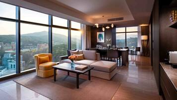 A modern hotel room with a large window, a sofa, a coffee table, and a dining area.