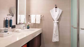 A modern bathroom with a marble sink, a large mirror, a robe hanging on a rack, and a glass shower enclosure.