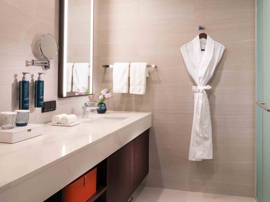A modern bathroom with a marble sink, a large mirror, a robe hanging on a rack, and a glass shower enclosure.