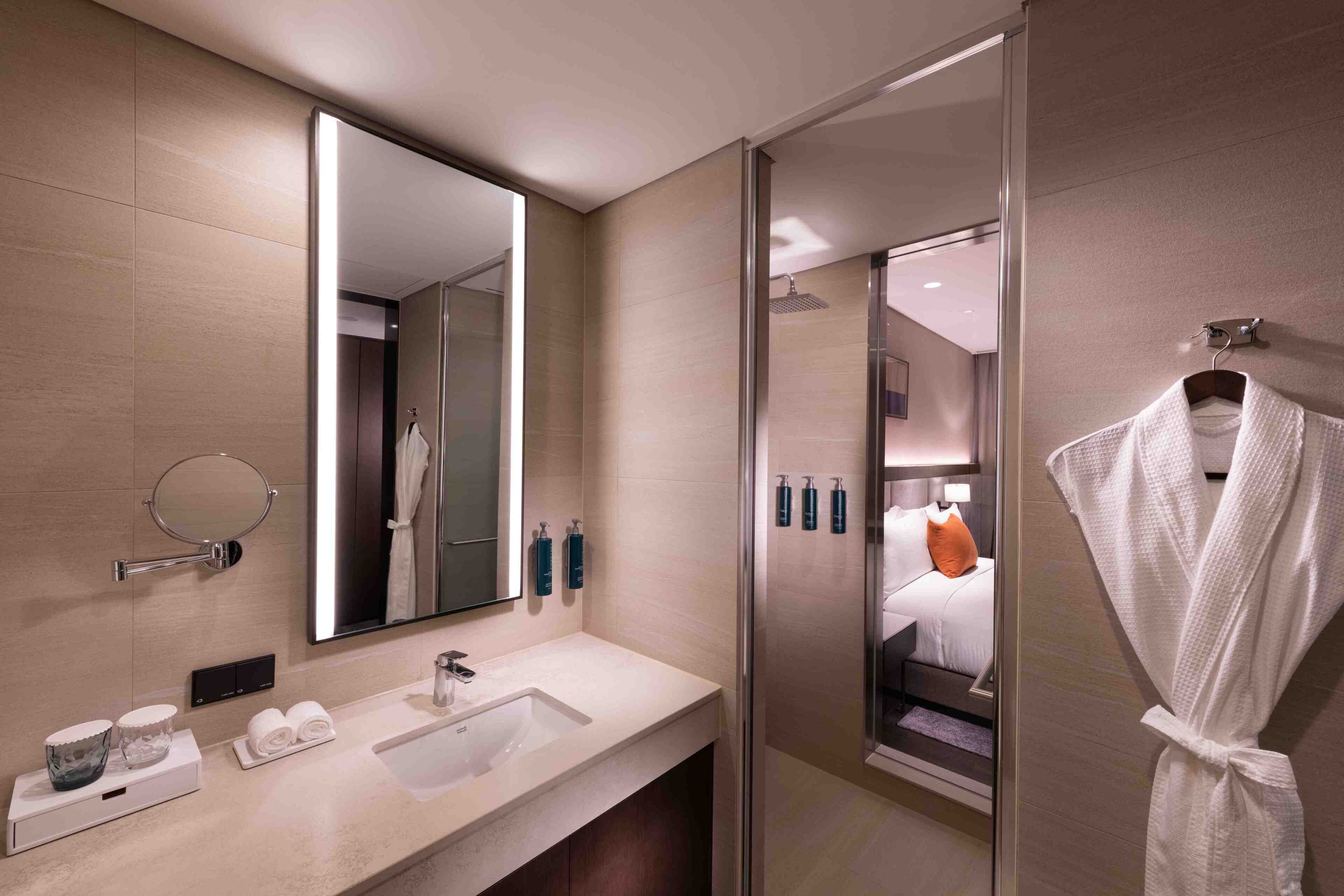 A modern bathroom with a large mirror, a sink, a glass shower enclosure, and a robe hanging on a hook.