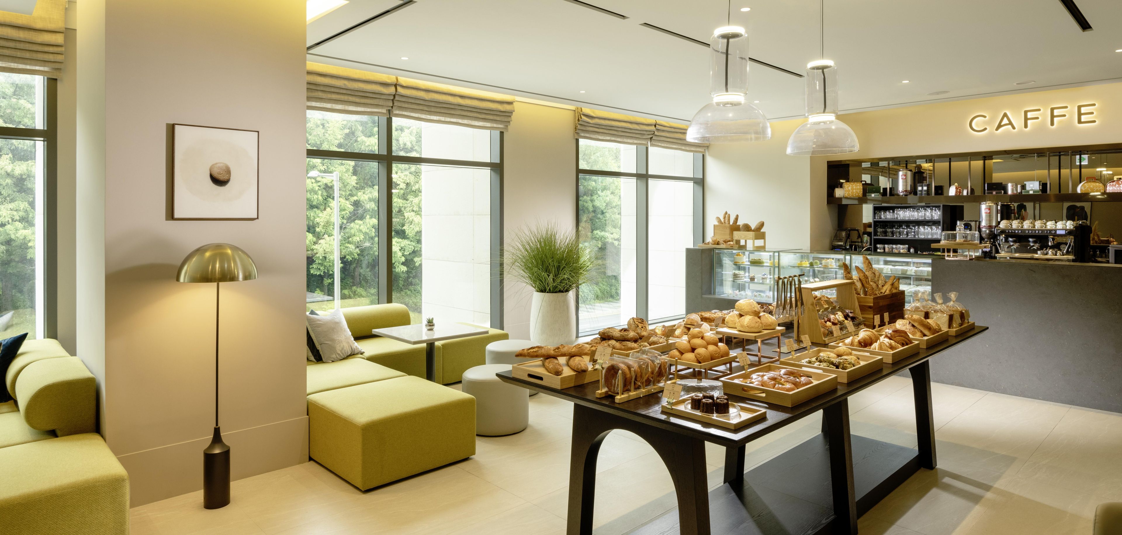 Um café com interior moderno, área de estar com sofás, vitrine de doces e um balcão com equipamentos para preparo de café.