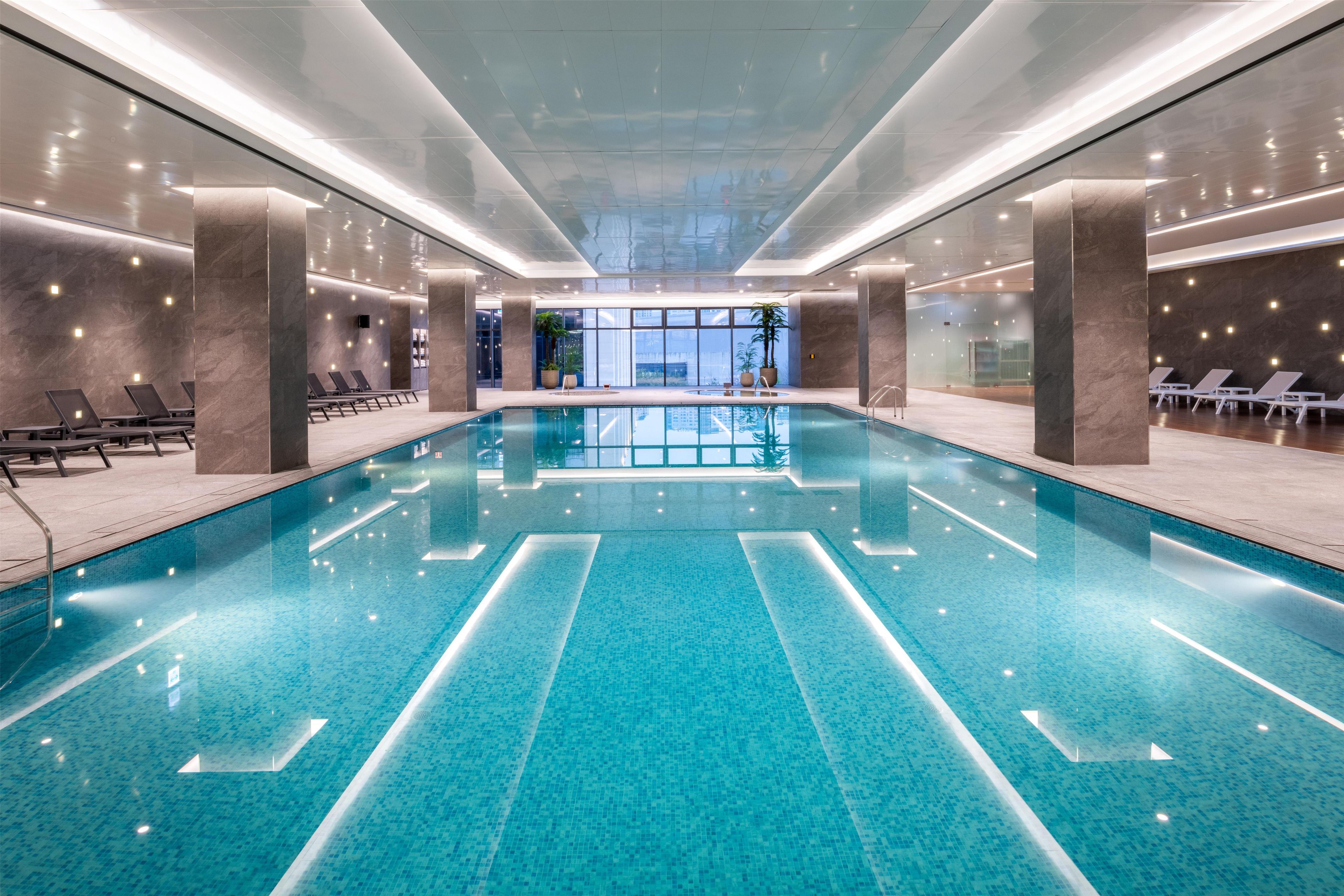 A large indoor swimming pool with clear blue water, surrounded by lounge chairs and modern architecture.