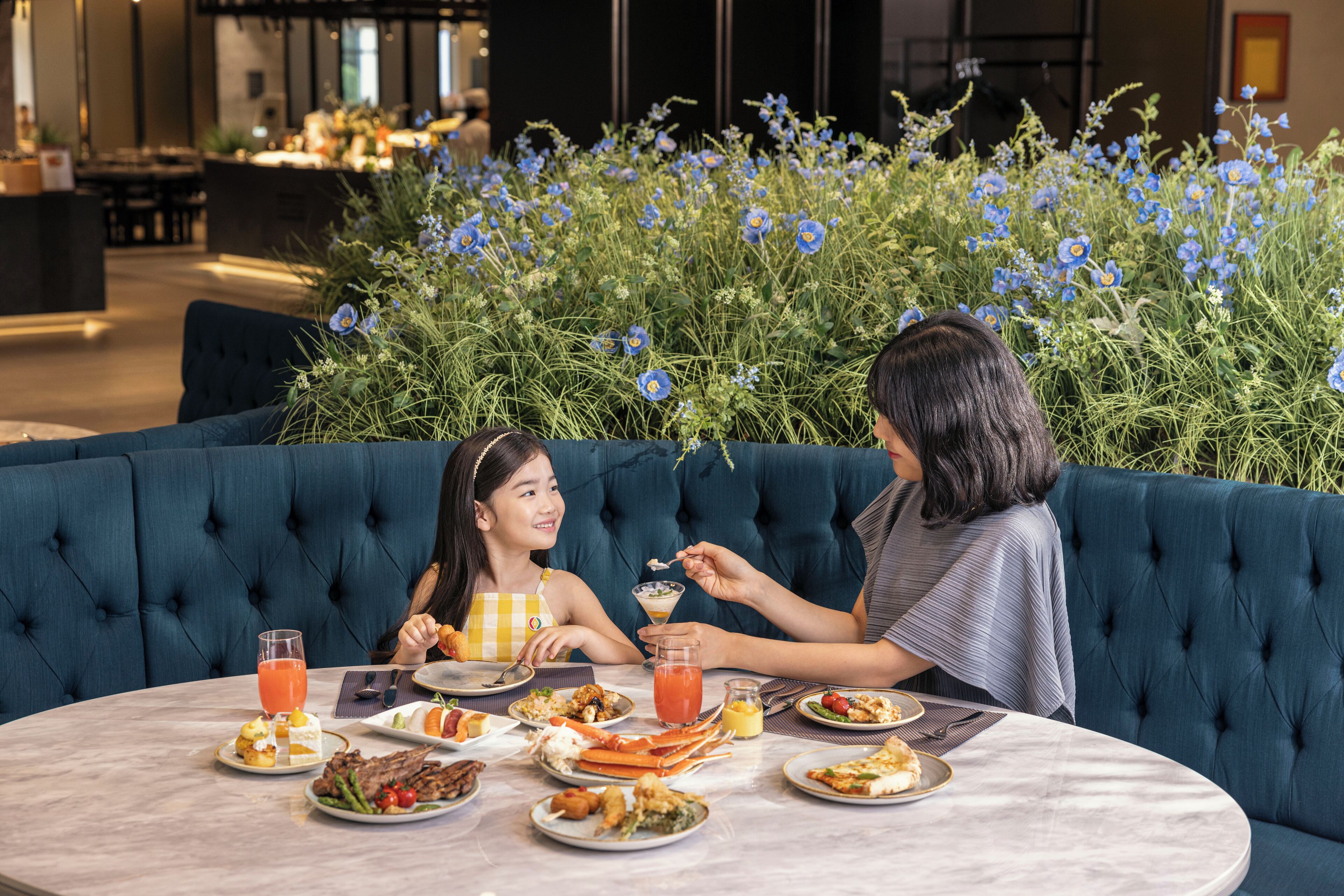 A dining area with a round table, blue upholstered seating, and a floral backdrop.