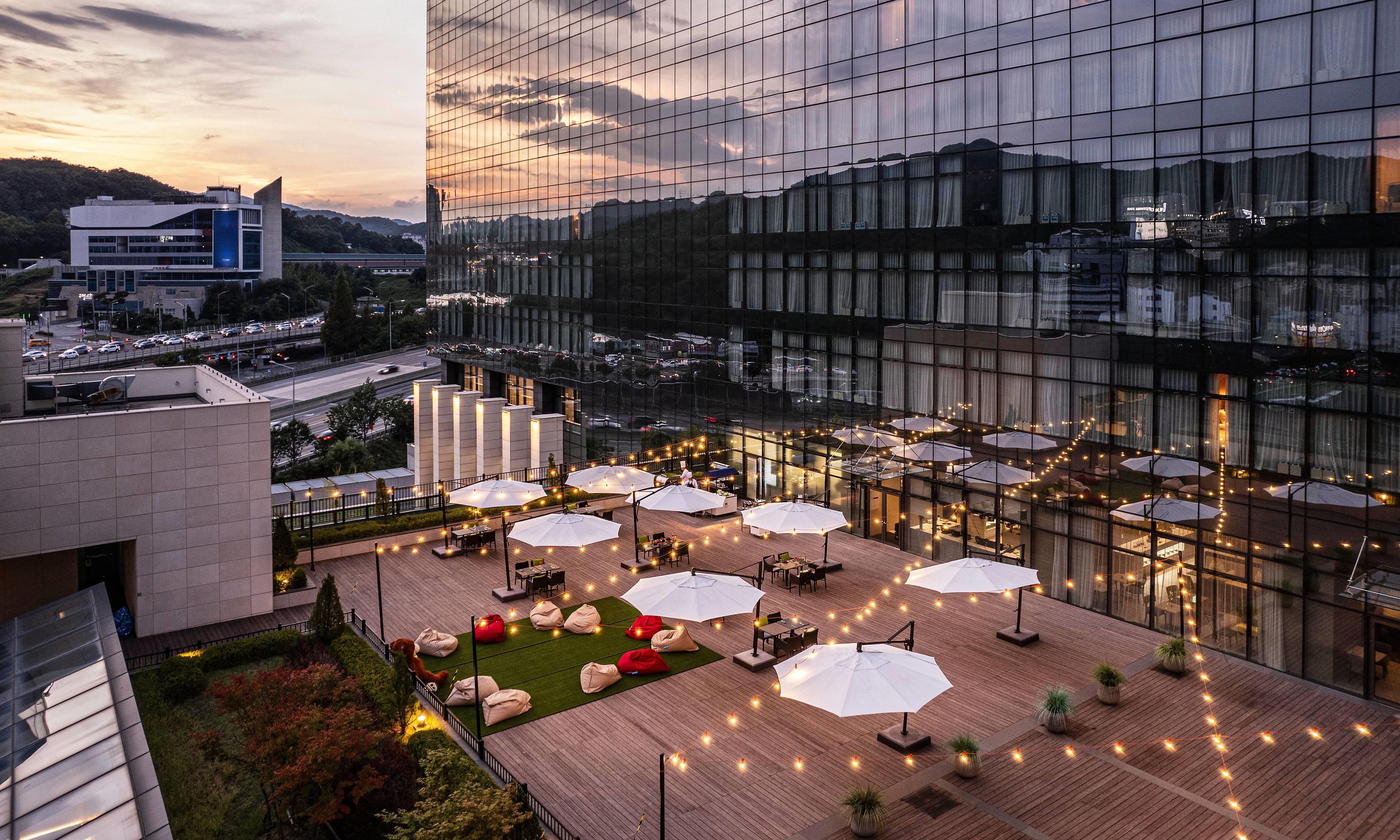 Una terraza en la azotea con mobiliario exterior y sombrillas, rodeada por un edificio moderno con ventanales de vidrio.