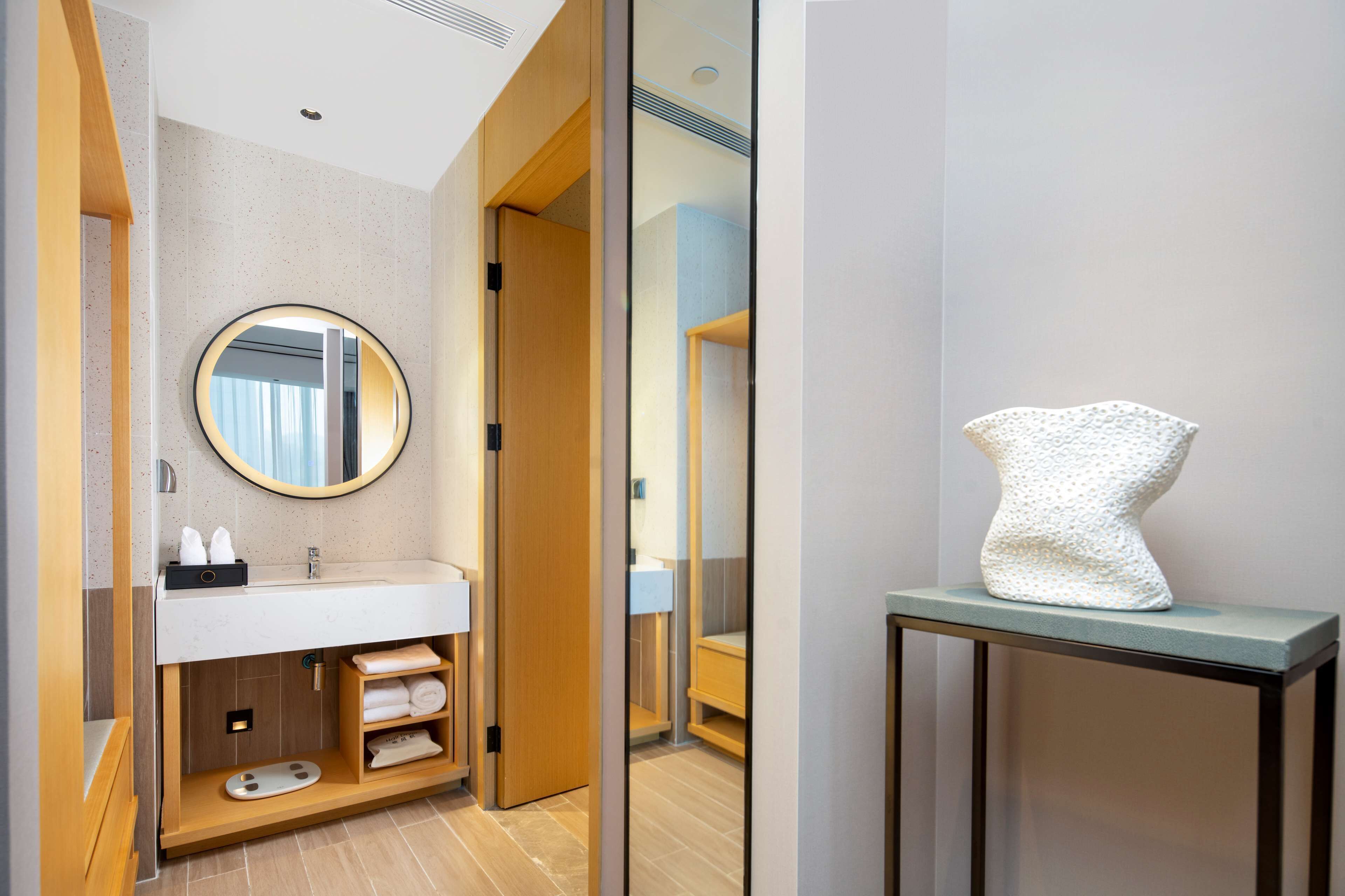 A modern bathroom with a round mirror, a sink, and a towel rack.