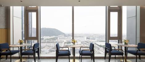 Una habitación de hotel moderna con ventanas amplias, una mesa redonda con sillas y vistas a la ciudad.