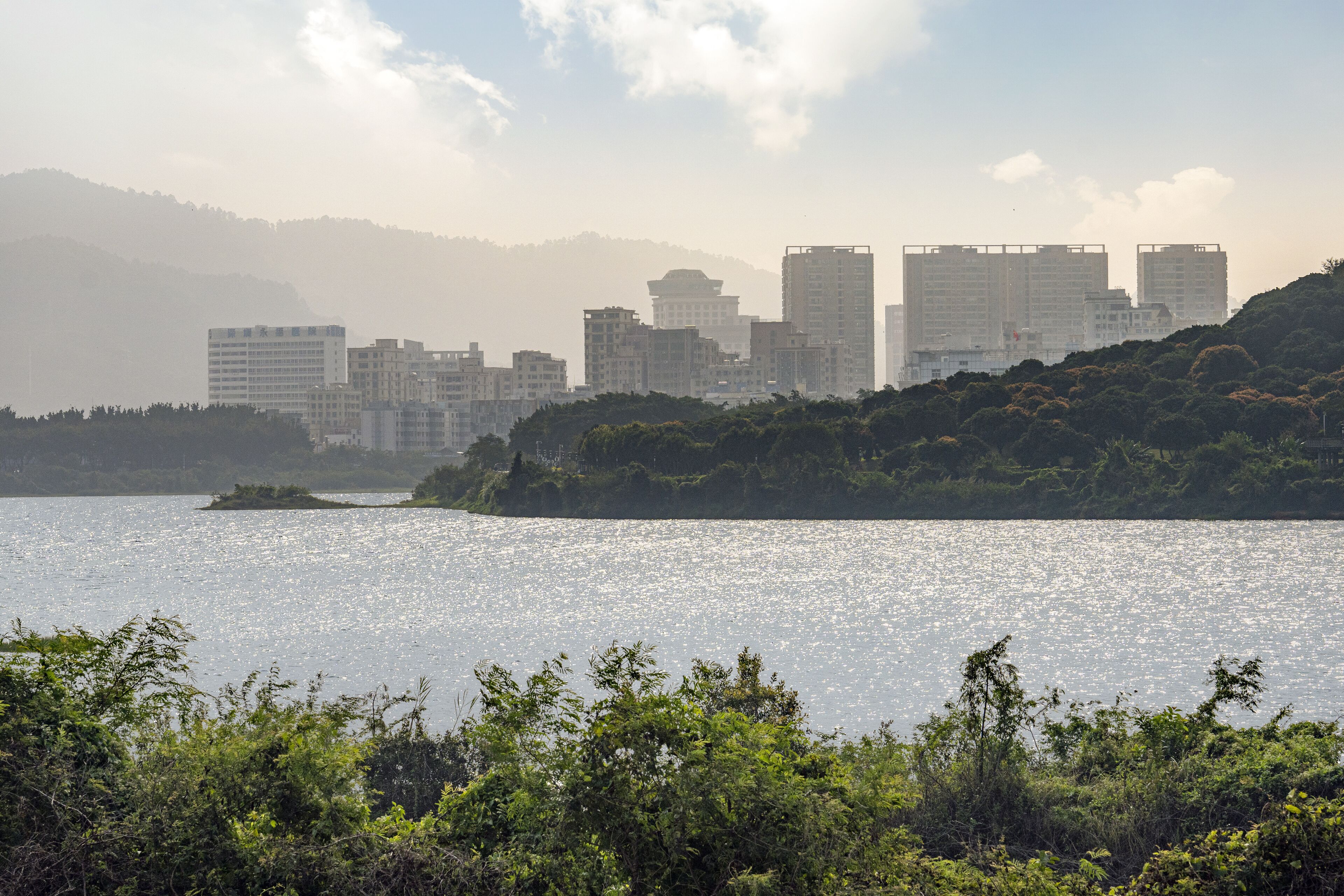 Silhueta urbana com edifícios modernos, um corpo de água e uma colina coberta de vegetação.
