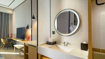A modern hotel bathroom with a large mirror, a sink, and a vanity area.