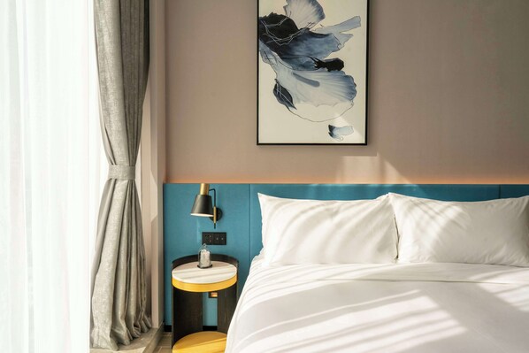 A hotel room with a bed, a bedside table, a lamp, and a painting on the wall. - Hilton Garden Inn Shenzhen Airport (Shenzhen)