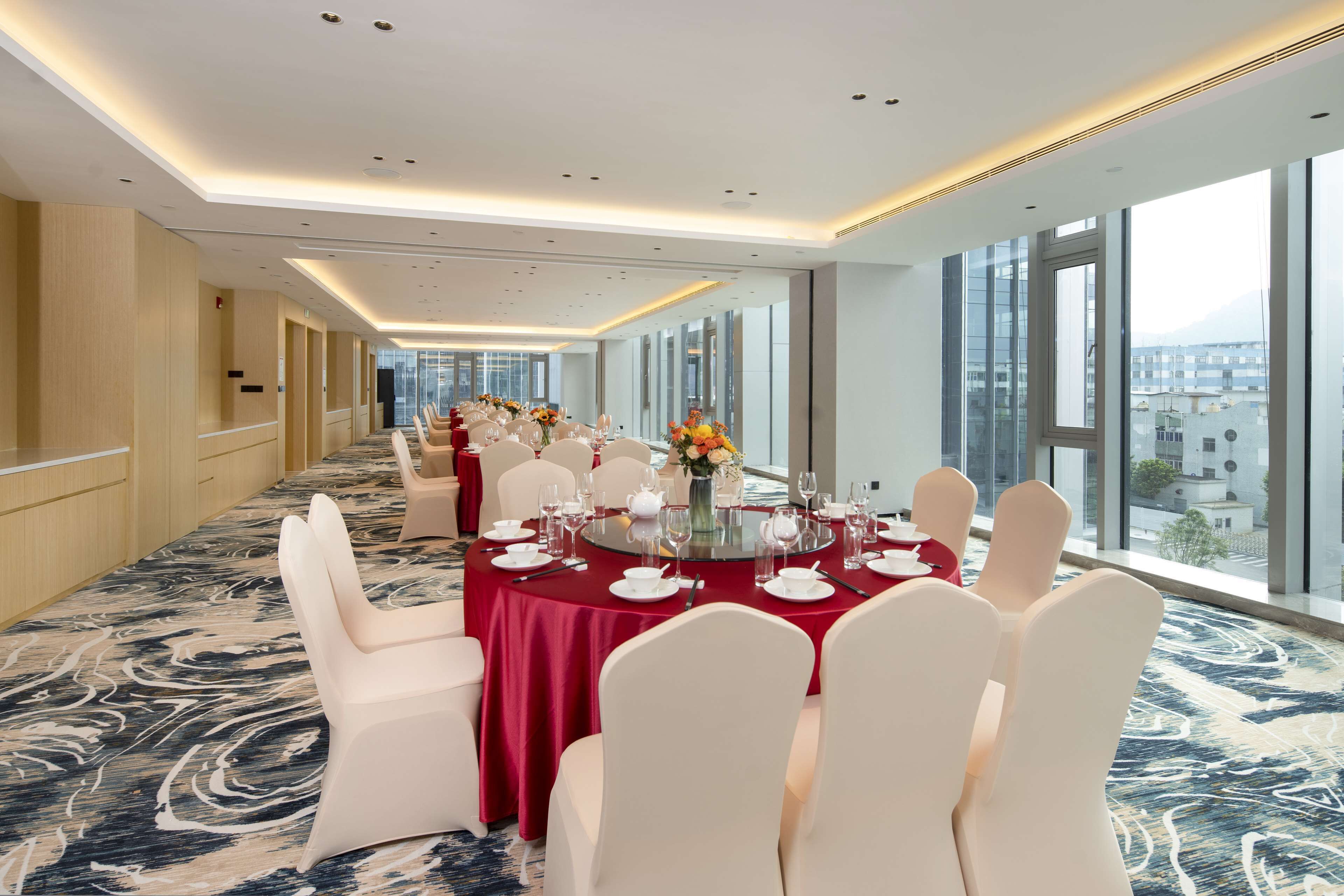 Une salle de conférence d’hôtel avec une longue table préparée pour une réunion, de grandes fenêtres et un aménagement intérieur moderne.