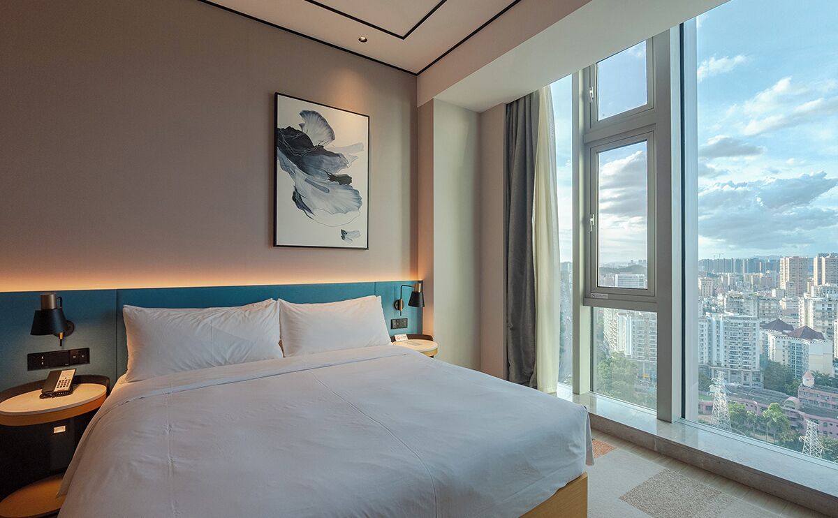 Una habitación de hotel moderna con una cama grande, vistas a la ciudad y un cuadro en la pared.