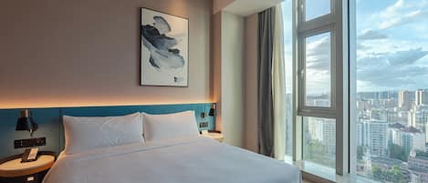 Ein modernes Hotelzimmer mit einem großen Bett, Blick auf die Stadt und einem Gemälde an der Wand.