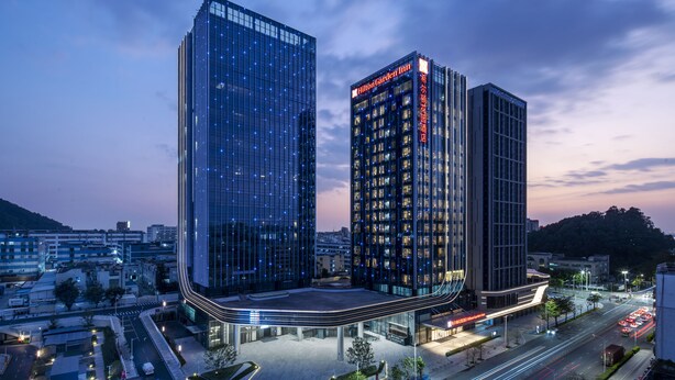 A modern hotel with a curved facade, multiple floors, and illuminated signage. - Hilton Garden Inn Shenzhen Airport (Shenzhen)