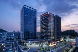 Un hôtel moderne à la façade incurvée, doté de plusieurs étages et d’une enseigne lumineuse.
