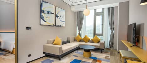 Et moderne hotelværelse med sofa, rundt sofabord, fjernsyn og kunst på væggen.