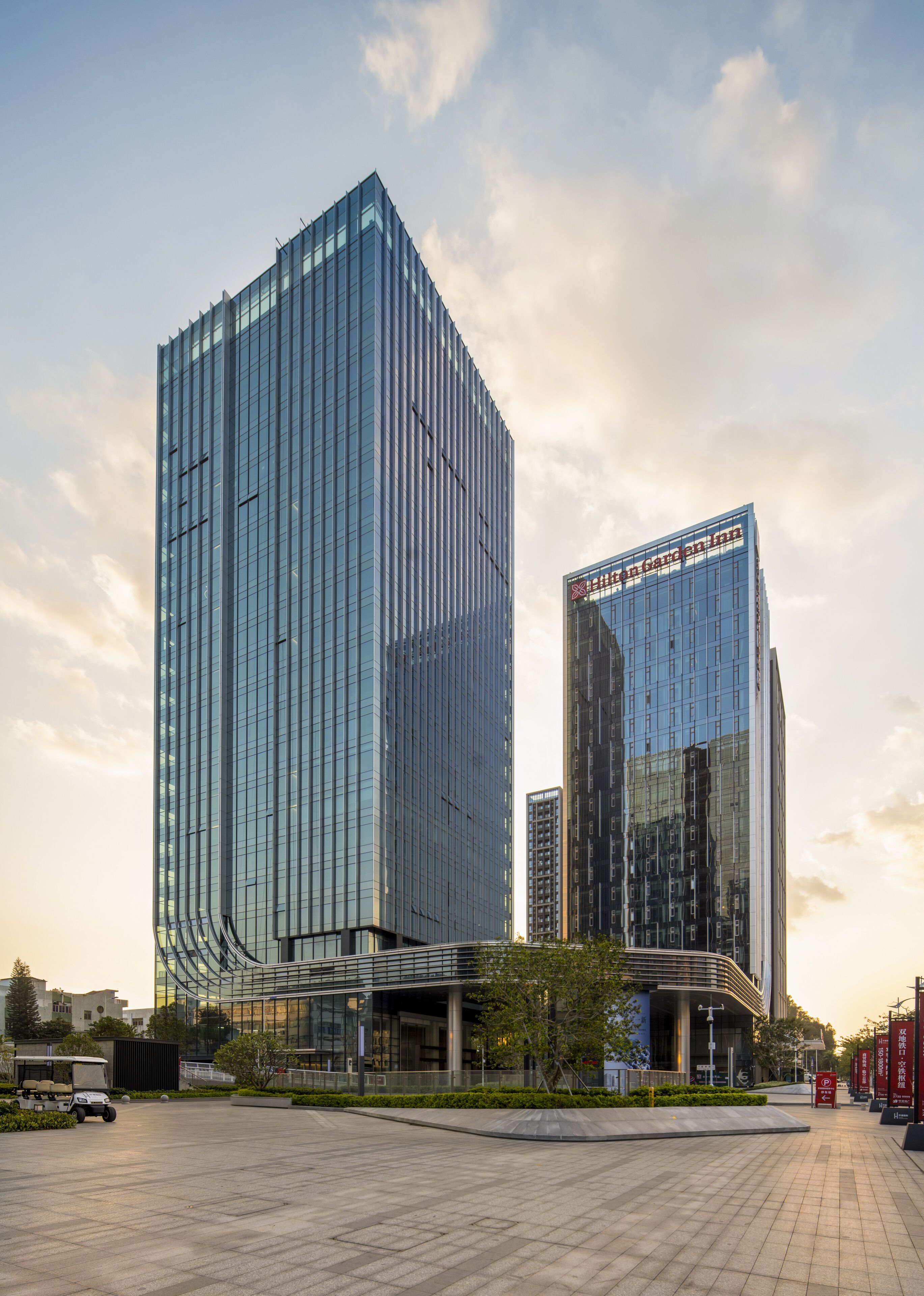 A modern hotel with a glass facade, a garden view, and a spacious outdoor area.