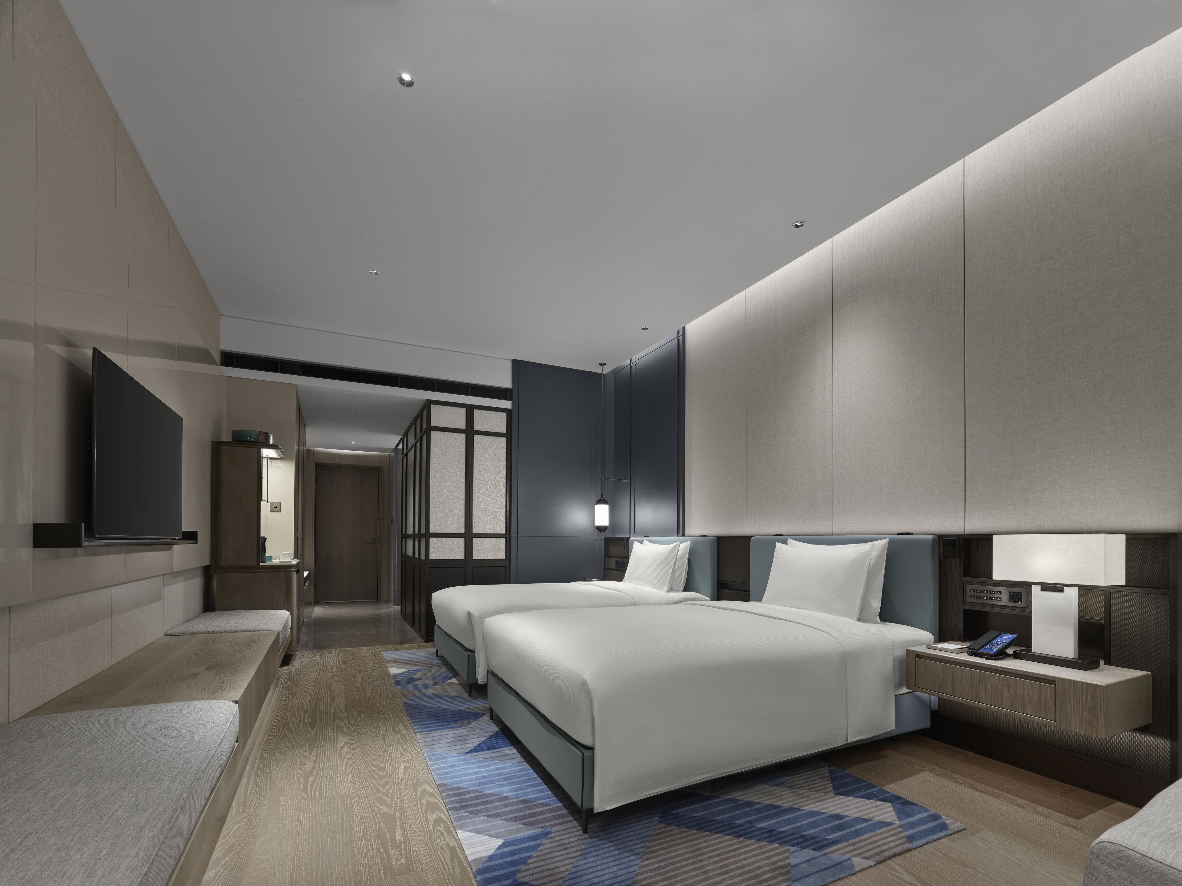 A modern hotel room with a large bed, bedside tables, a flat-screen TV, and a walk-in closet.