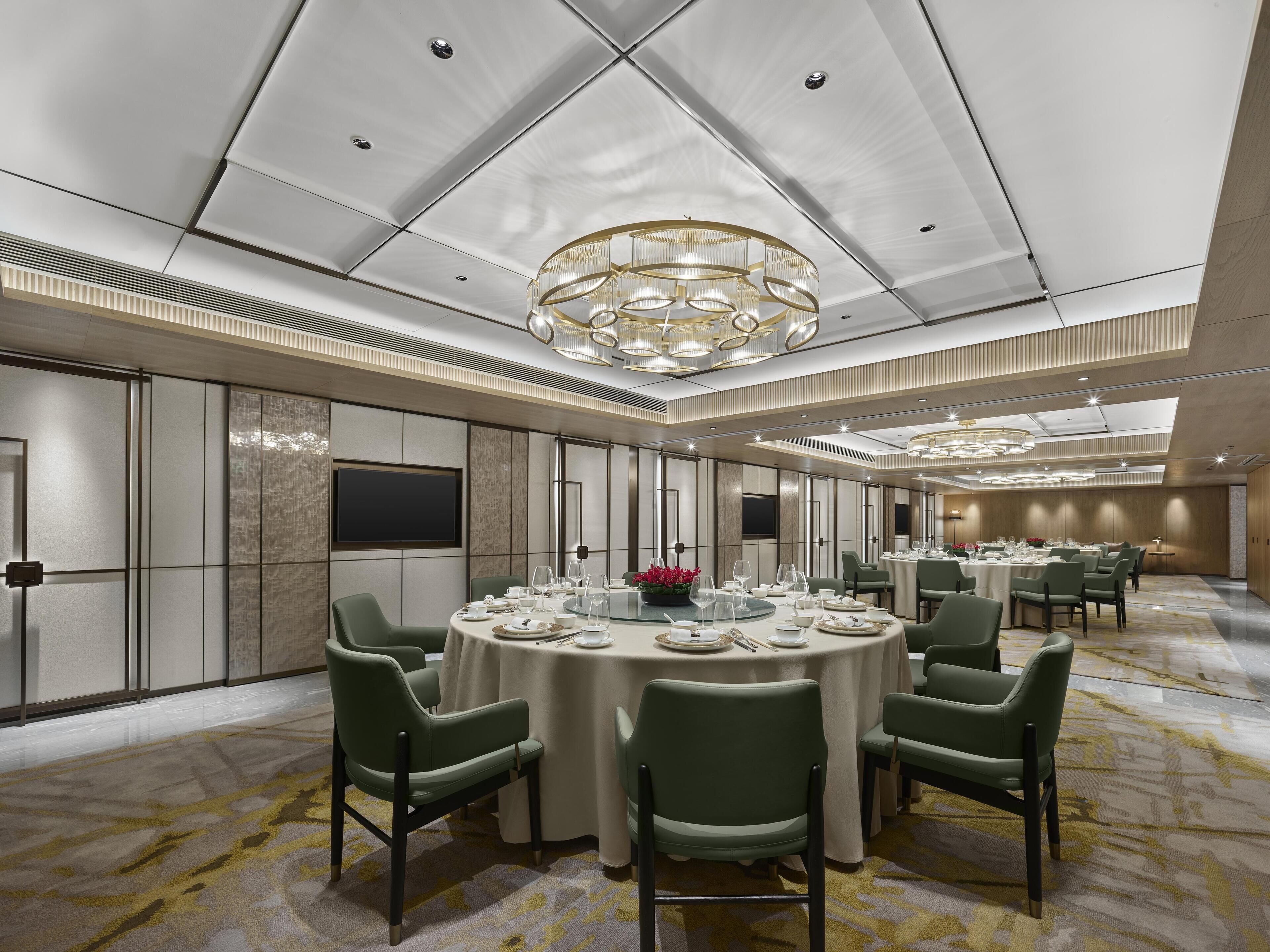 A modern conference room with a round table, green chairs, and a chandelier.