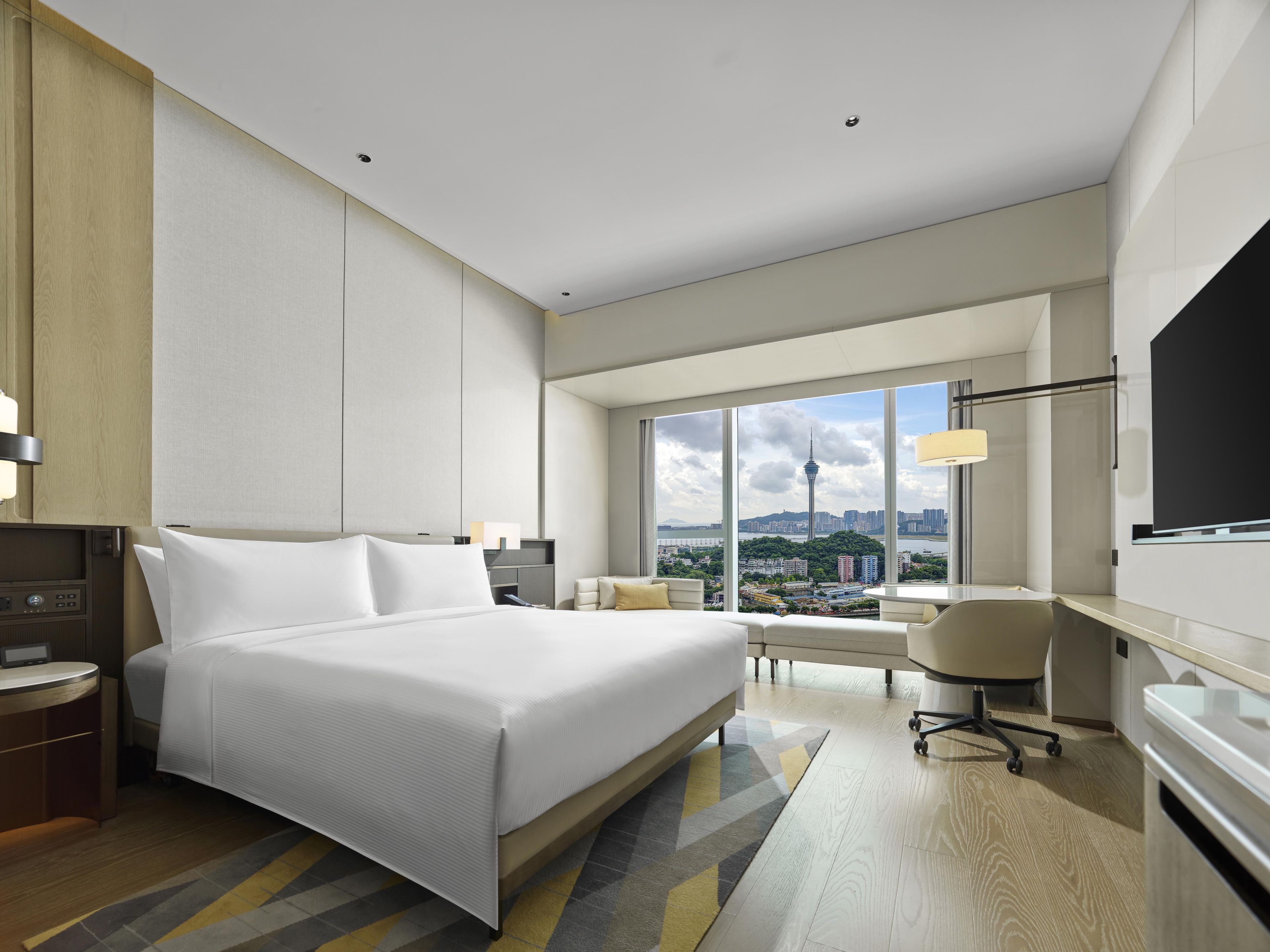 A modern hotel room with a large bed, a desk, a chair, and a television.