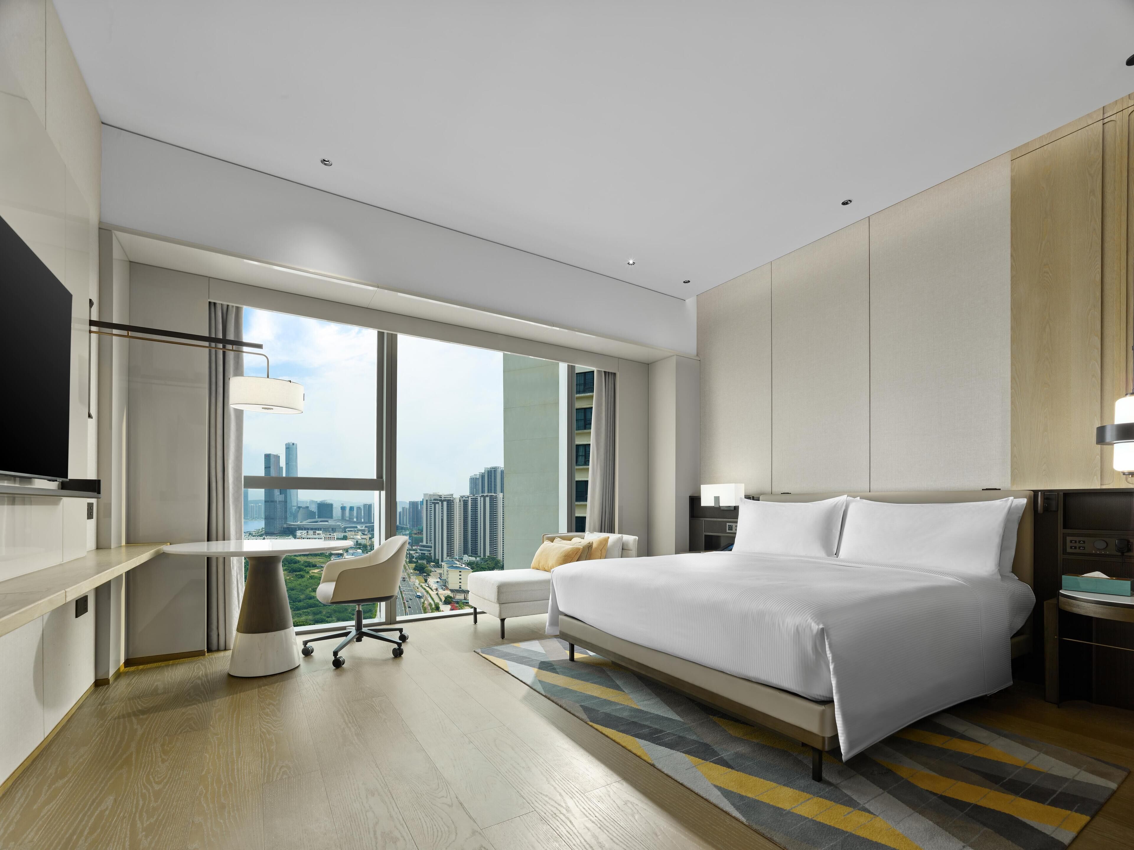 A modern hotel room with a large bed, a desk, a chair, and a TV.