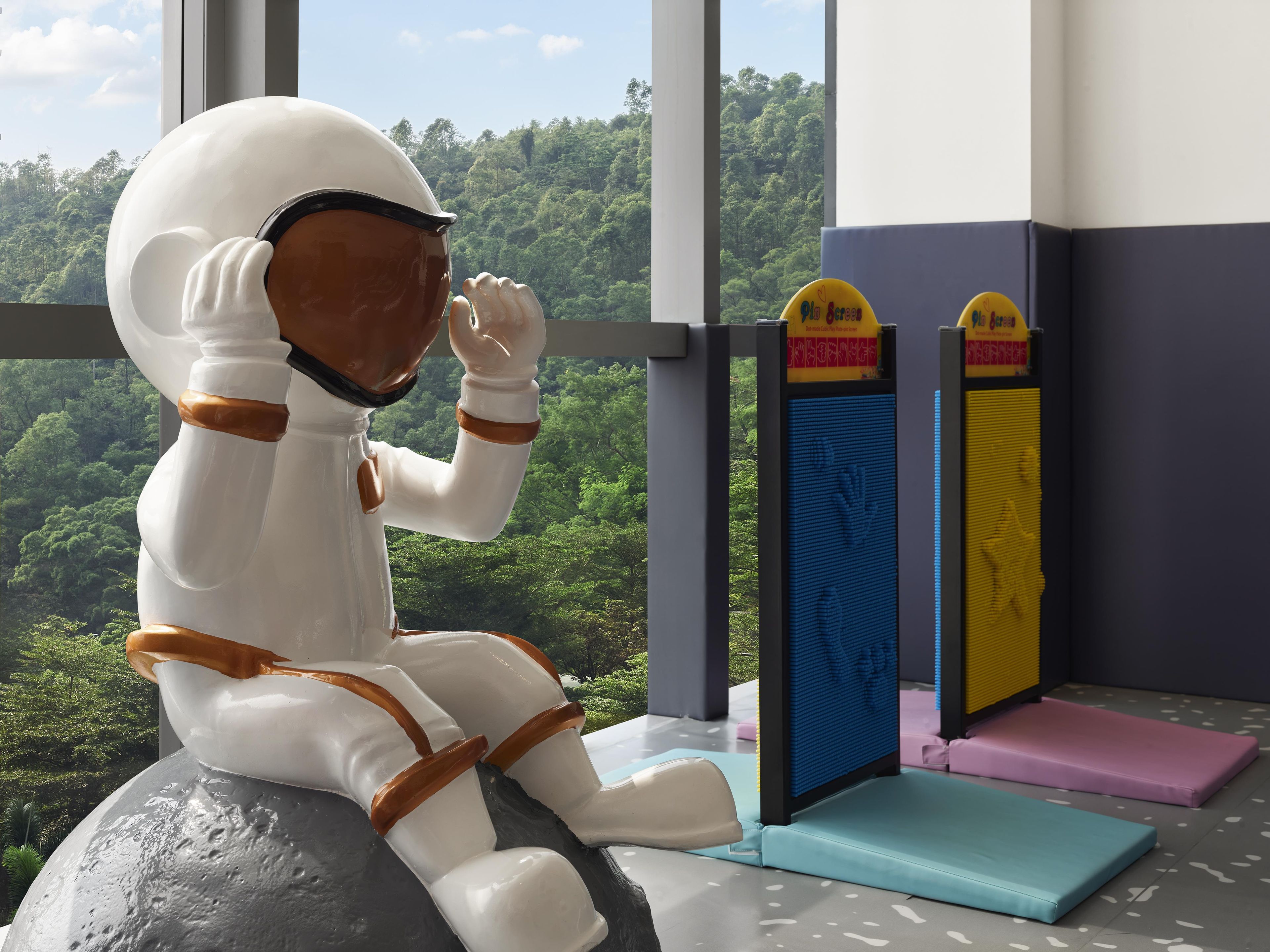 A space-themed sculpture of an astronaut sitting on a rock, with a view of a forest through a window.