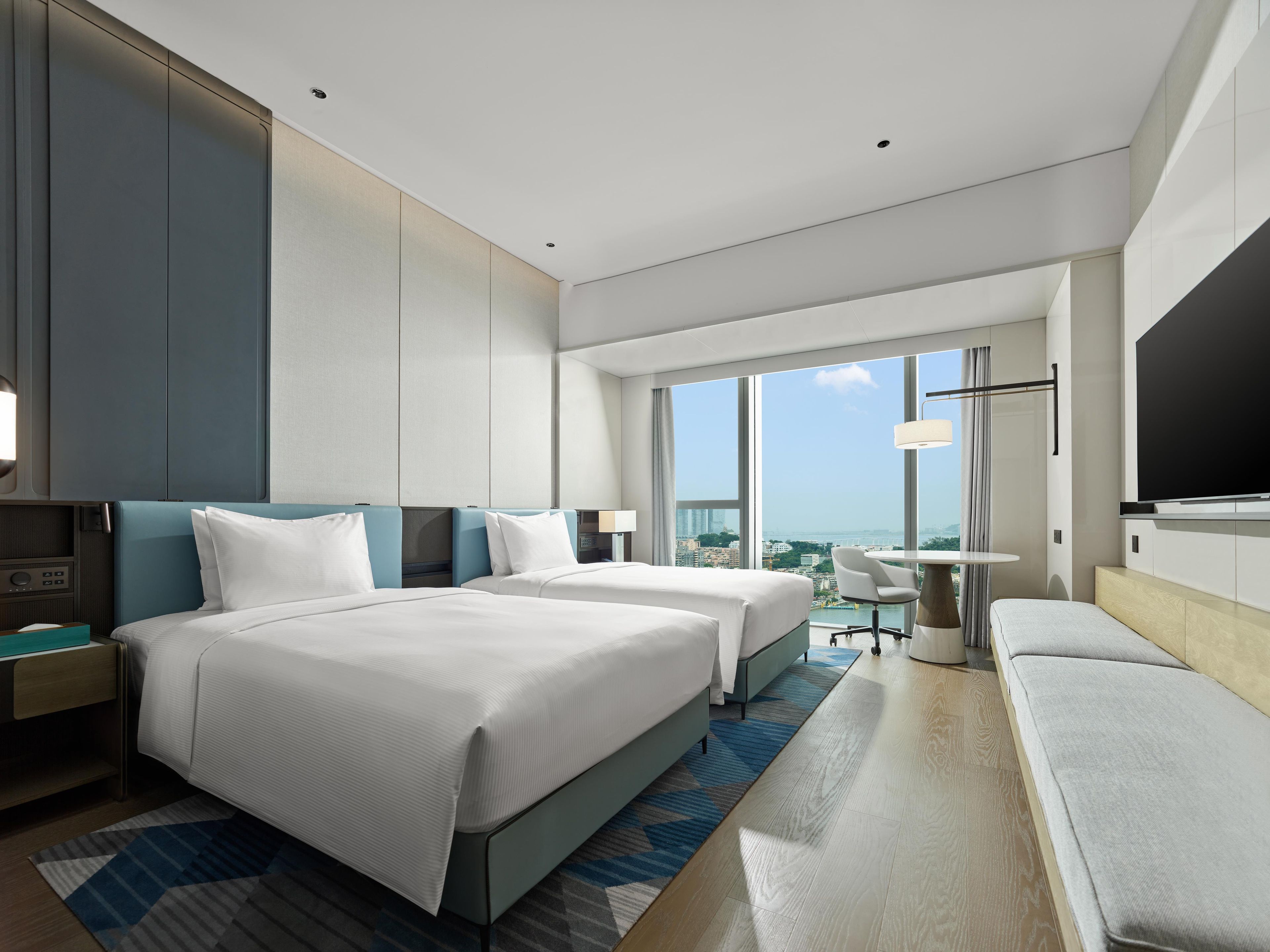 Habitación de hotel moderna con dos camas, un televisor de pantalla plana, un escritorio y vistas a la ciudad.