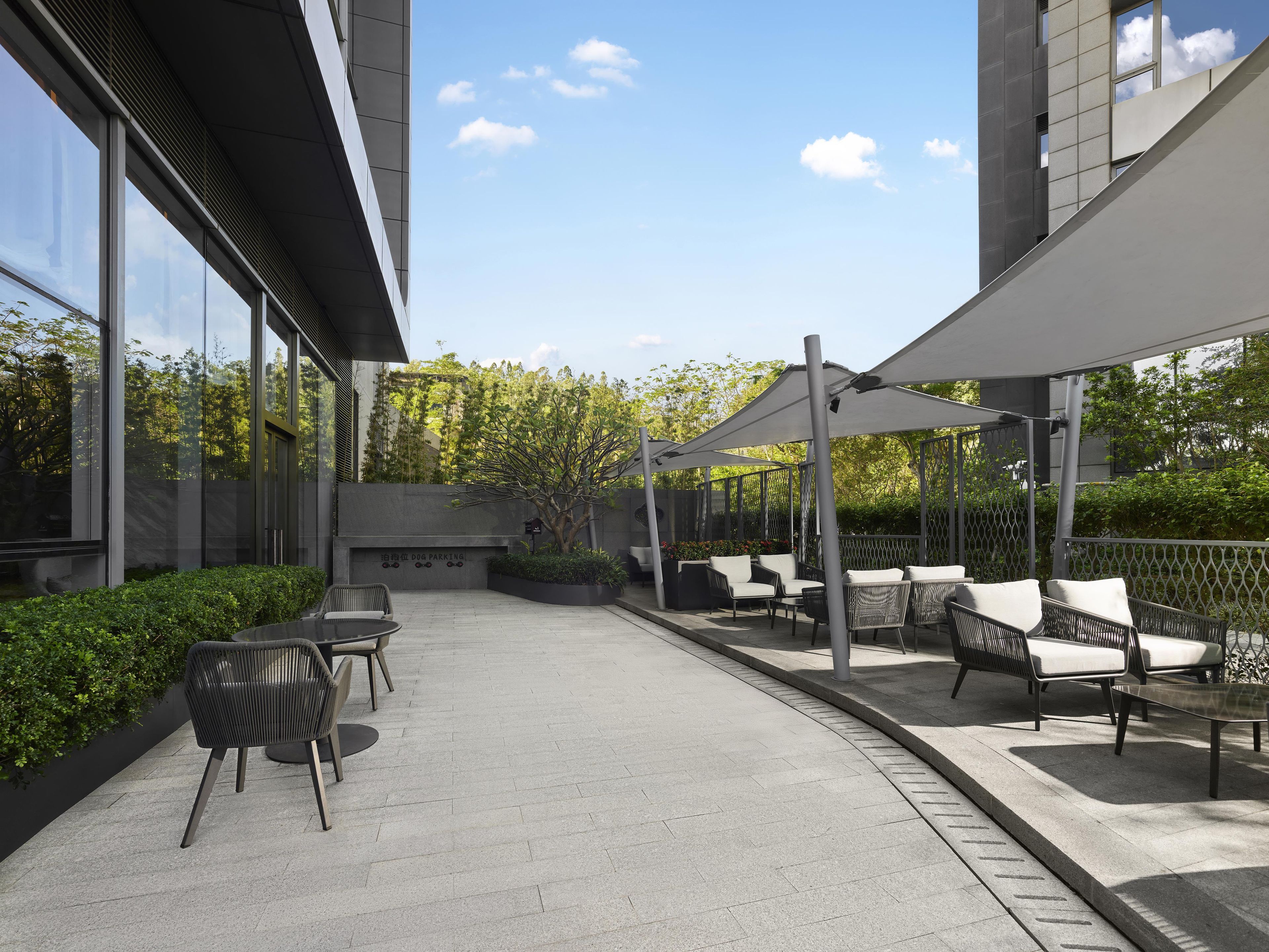 Un patio al aire libre con asientos y un toldo sombreado, rodeado de follaje y arquitectura moderna.