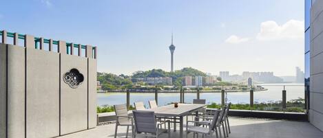 An outdoor terrace with a table and chairs, a view of a river, and a cityscape in the background.