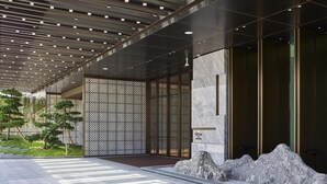 Una entrada de hotel moderna con un paseo techado, una característica decorativa de rocas y una valla con diseño.