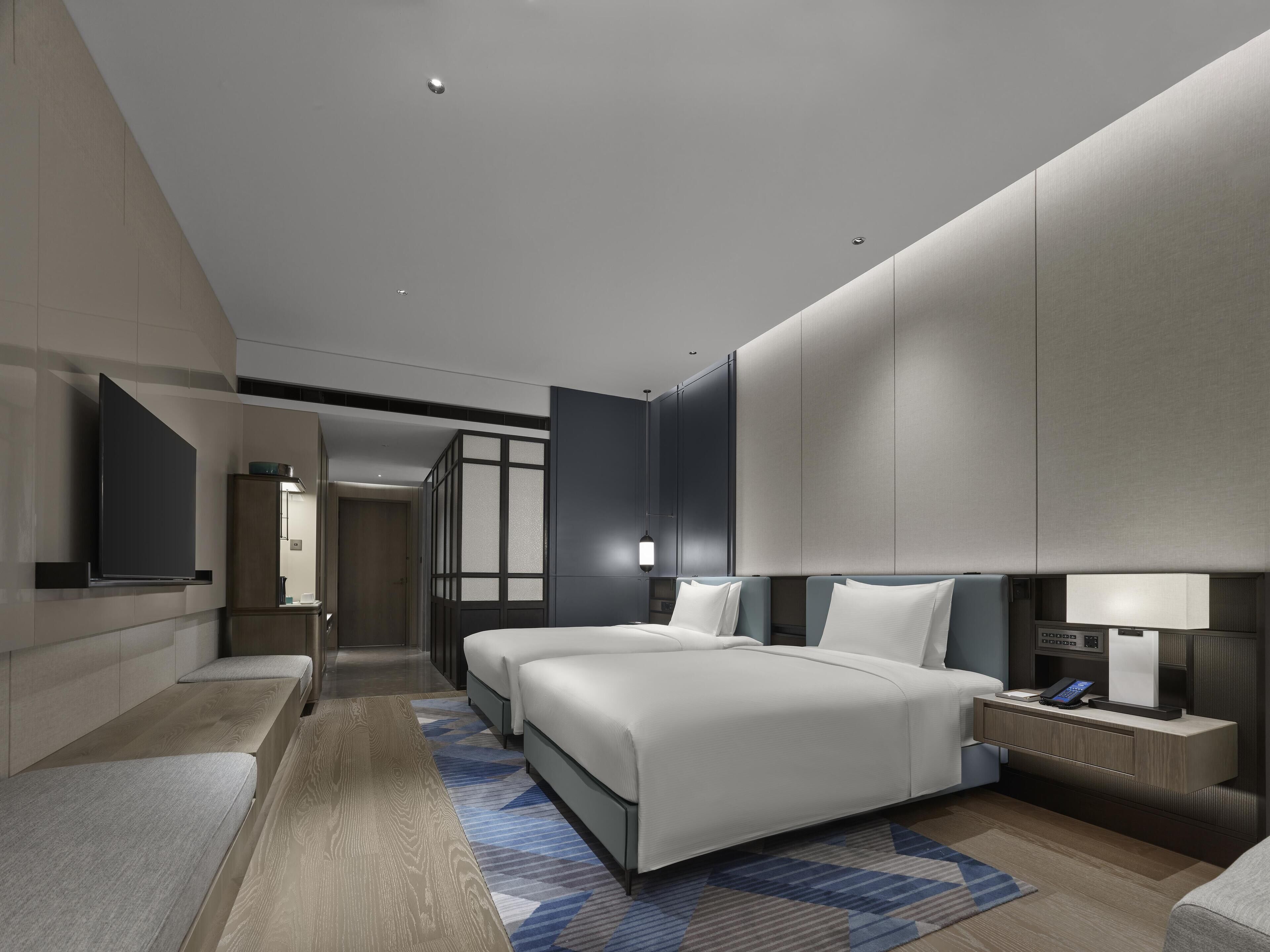 A modern hotel room with a large bed, bedside tables, a flat-screen TV, and a walk-in closet.