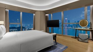 Una habitación de hotel moderna con una cama grande, televisión, espejo redondo y vistas a la ciudad y al agua.