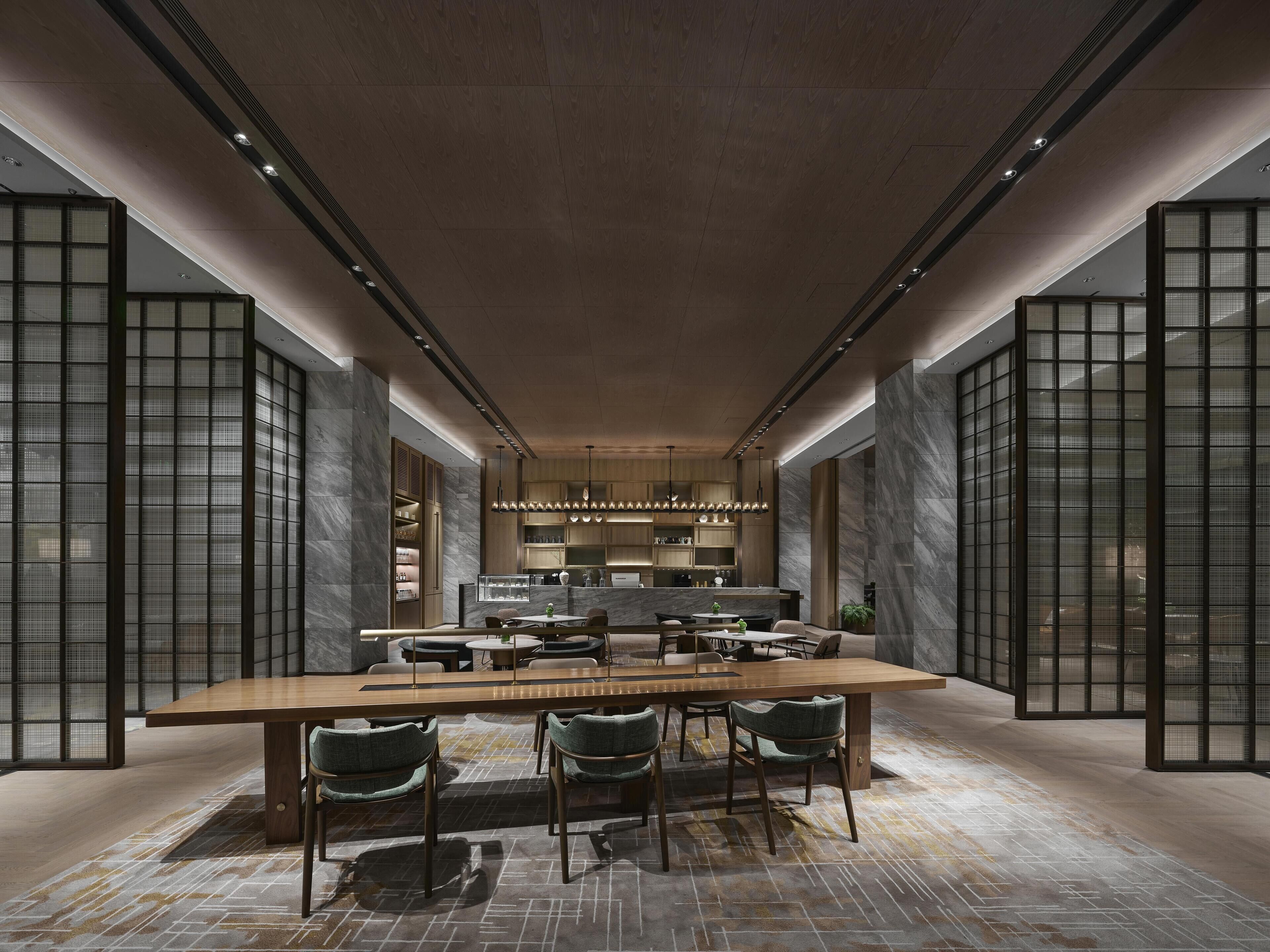 Un espace de salle à manger moderne avec une longue table et des chaises, une cuisine en arrière-plan et un sol à motifs.