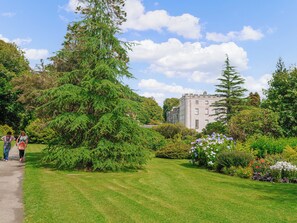 A lush garden with a large coniferous tree, a well-maintained lawn, and a historic building in the background.