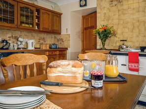 A kitchen with wooden cabinets, a dining table with a loaf of bread, a glass of juice, and a jar of jam.