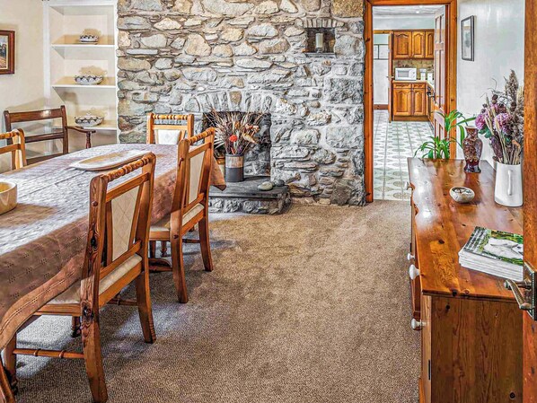 A dining area with a stone wall, wooden chairs, a table, and a kitchen in the background.