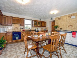 A kitchen with wooden cabinets, a dining table with chairs, a microwave, and a stove.